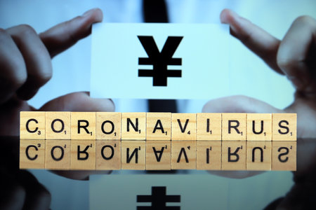 WROCLAW, POLAND - MARCH 30, 2020: The word CORONAVIRUS made of wooden letters, and man holding a business card with yen or yuan sign in the background. Coronavirus (COVID-19) global disease 2020.のeditorial素材