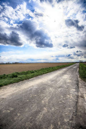 Empty, local road among fields on a stormy day on the last days of April. Spring landscape with beautiful clouds.の写真素材