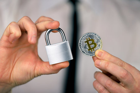 A businessman holds a silver padlock and physical version of bitcoin in his hands. Prohibition of cryptocurrencies, regulations, restrictions or security, protection, privacy.の写真素材