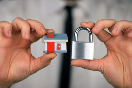 A businessman in a white shirt and black tie holds a silver padlock and miniature house in his hands. home security.の写真素材