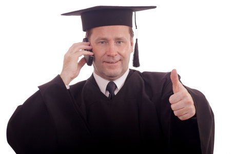Man in graduation gown talking on the phone while showing thumbs up