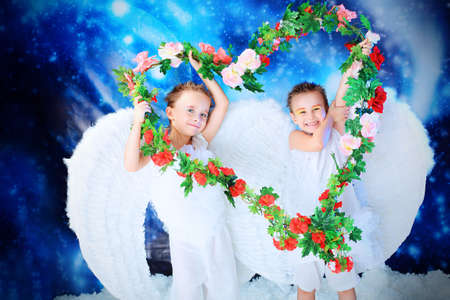 Beautiful little angels holding heart of flowes at a snowy background.の写真素材