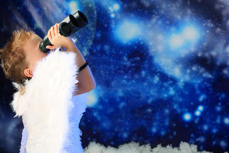 Beautiful little angel looking through his binocular,  snowy background.の写真素材