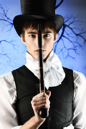 Portrait of a young gentlemen in a jacket top hat holding gun in his hand. Shot in a studio.の写真素材