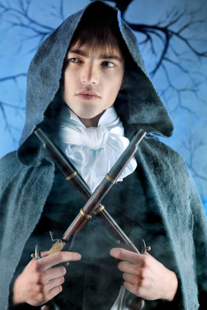 Portrait of a young gentlemen in a dinner jacket and cloak holding guns in his hands. Shot in a...