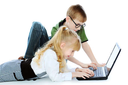 Shot of a little girl and boy lying on a floor with a laptop. Isolated over white background.の写真素材