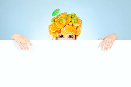 Shot of a beautiful young woman with fruits headwear holding white board. Food concept, healthcare.の写真素材