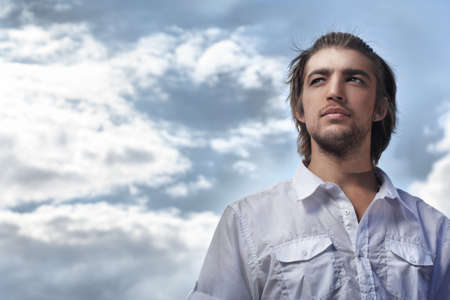 Handsome young man posing over blue sky.の写真素材