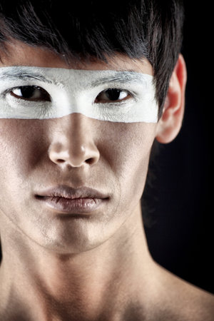 Shot of a stylish young man with painted eyes posing over black background.の写真素材