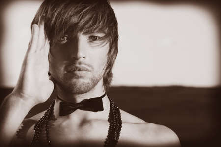 Fashion shot of a handsome young man posing topless in top hat and bow tie over beautiful landscape.の写真素材