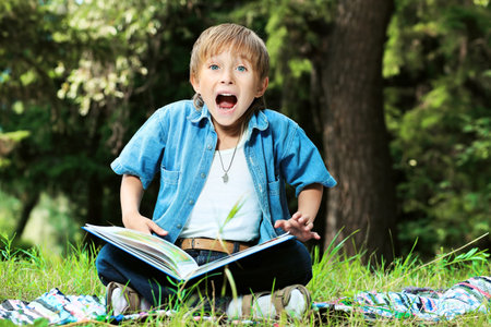 Shot of a little boy with a book having a rest outdoor.の写真素材