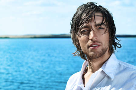 Handsome young man posing over sea and blue sky.の写真素材