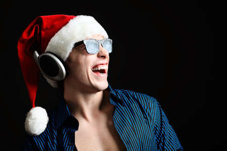 Portrait of a funny young man in Santa Claus hat and headphones. Christmas.の写真素材