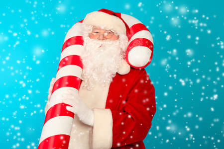 Portrait of Santa Claus with big candy over blue background. Christmas.の写真素材