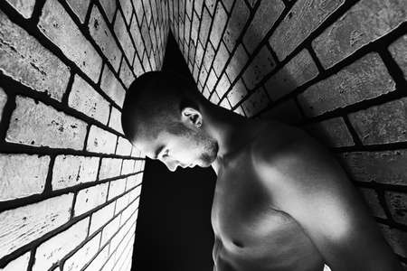 Portrait of a handsome muscular man posing over black background and brick wall.の写真素材