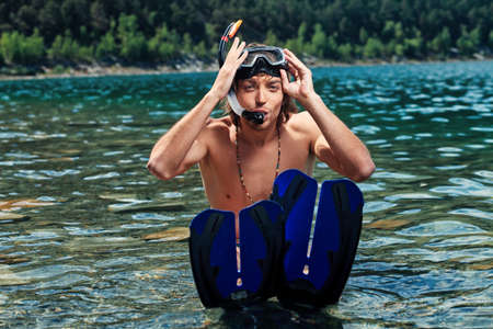 Happy young man with snorkelling gear sitting in a sea.の写真素材