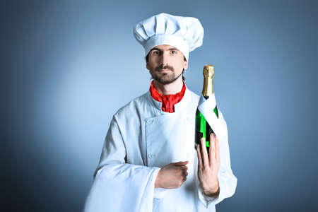 Portrait of a man cook holding a bottle of champagne. Shot in a studio over grey background.の写真素材
