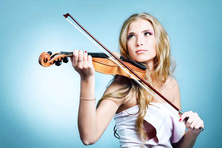 Beautiful young woman playing her violin with expression. Over grey bakground.の写真素材