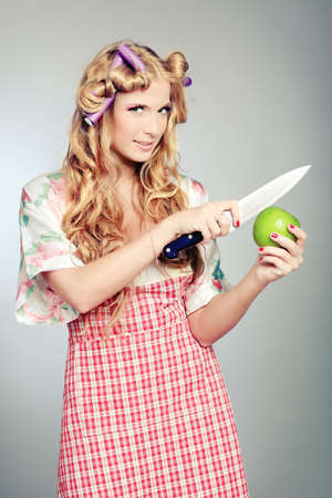 Beautiful blonde woman housewife holding apple and a knife. Studio shot over grey background.の写真素材