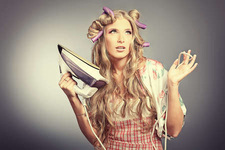 Portrait of a pretty young woman wearing a house dress and holding iron. Studio shot.の写真素材