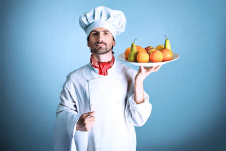 Portrait of a man cook holding a plate with fruits. Shot in a studio over grey background.の写真素材