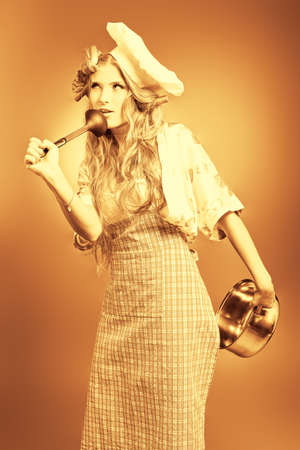 Beautiful blonde woman housewife holding pan. Studio shot over grey background.の写真素材