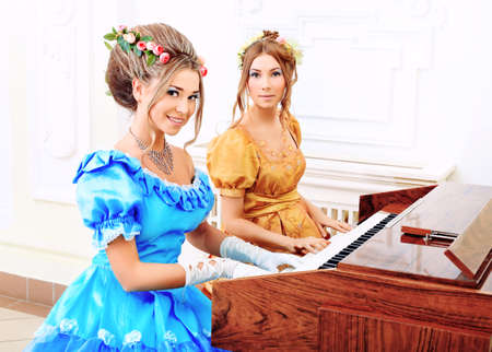 Two beautiful women in medieval era dresses playing the piano.の写真素材