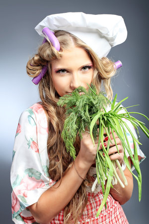 Beautiful blonde woman housewife holding greens and fruits. Studio shot over grey background.の写真素材