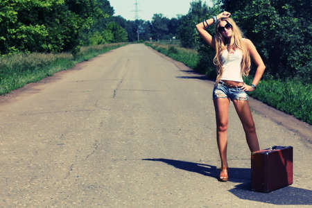 Pretty young woman hitchhiking along a road.の写真素材
