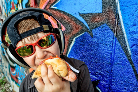 Portrait of a modern boy teenager eating hot dog outdoors.の写真素材