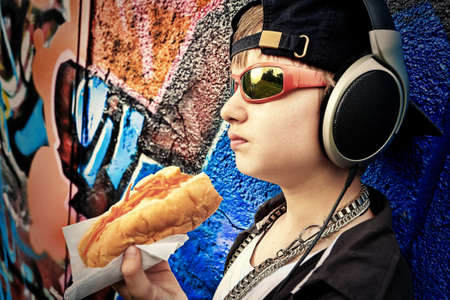 Portrait of a modern boy teenager eating hot dog outdoors.の写真素材