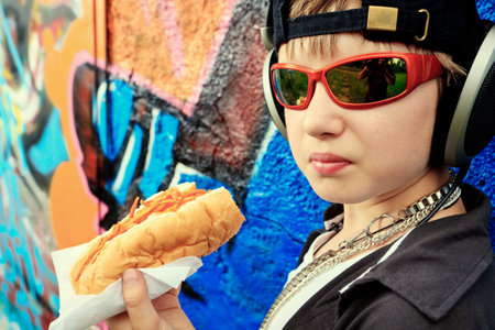 Portrait of a modern boy teenager eating hot dog outdoors.