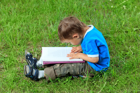 Shot of a little boy with a book having a rest outdoor.