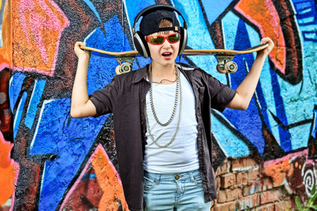 Portrait of a trendy boy teenager with headphones and skateboard outdoors.