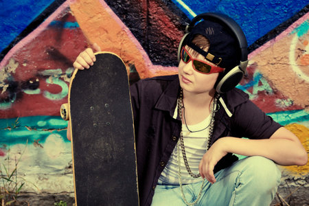 Portrait of a trendy boy teenager with headphones and skateboard outdoors.