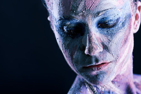 Portrait of an artistic woman painted with clay. Shot in a studio over black background. 