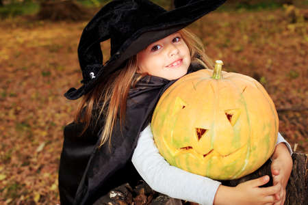 Shot of a little girl in halloween costume posing with pumpkin outdoor.の写真素材
