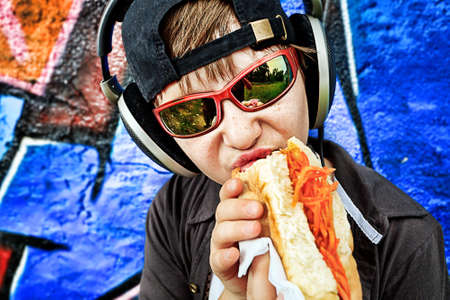 Portrait of a modern boy teenager eating hot dog outdoors.の写真素材