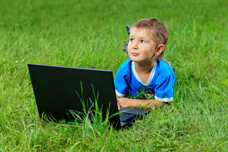 Portrait of a little boy lying with his laptop on a grass at a park.の写真素材
