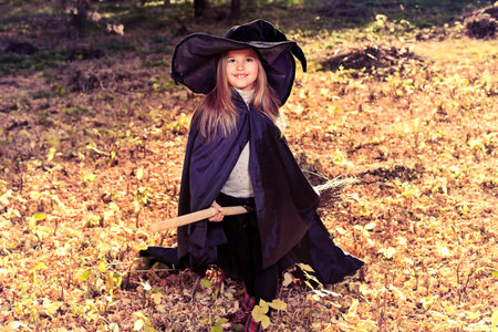 Shot of a little girl in halloween costume posing with broom and pumpkin outdoor.