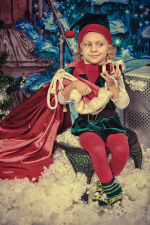 Little girl in Christmas elf costume posing over christmas background.