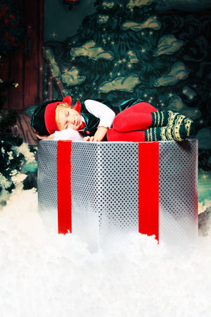 Little girl in Christmas elf costume posing over christmas background.