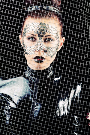 Conceptual shot of a woman in black glossy overall and metal buttons on her face.