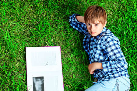Shot of a  teenager boy with a book having a rest outdoor.の写真素材