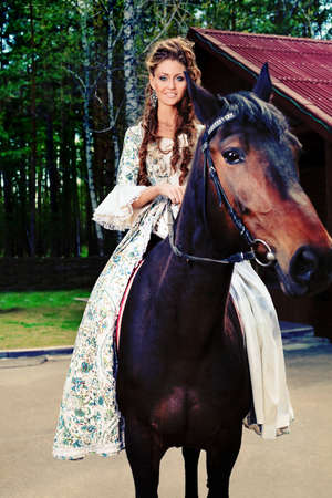 Beautiful young woman in medieval dress riding a horse outdoor.の写真素材