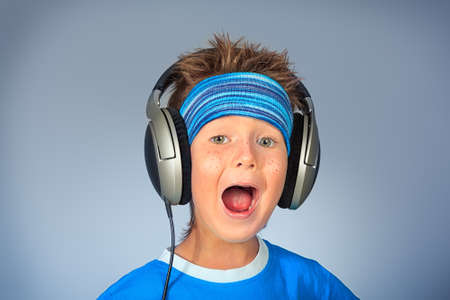 Portrait of a cute boy listening to music on headphones over grey background.の写真素材