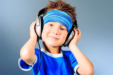 Portrait of a cute boy listening to music on headphones over grey background.の写真素材