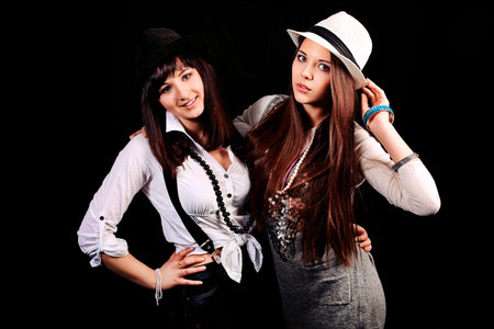 Two stylish young women posing over black background. 