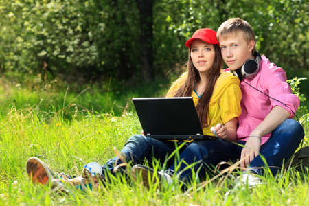 Couple of modern teenagers sitting with a laptop outdoors.の写真素材