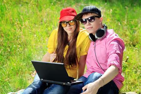 Couple of modern teenagers sitting with a laptop outdoors.の写真素材